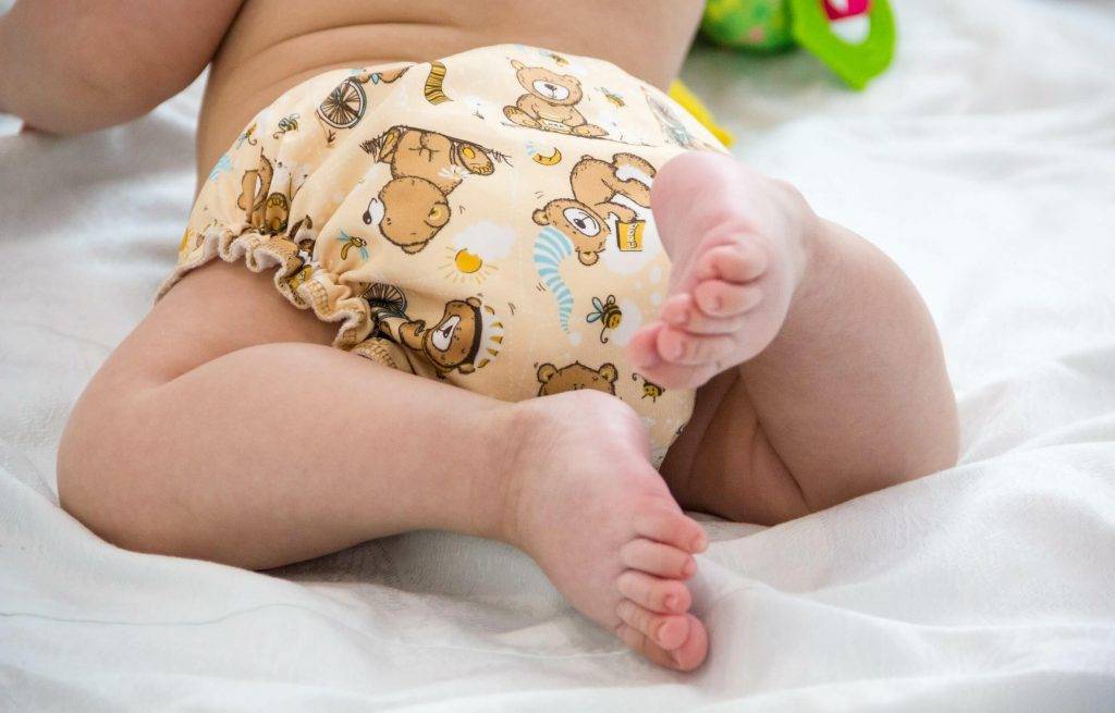 Baby von hinten mit strampelnden Füßen mit einer Stoffwindel in Bärenmotiv